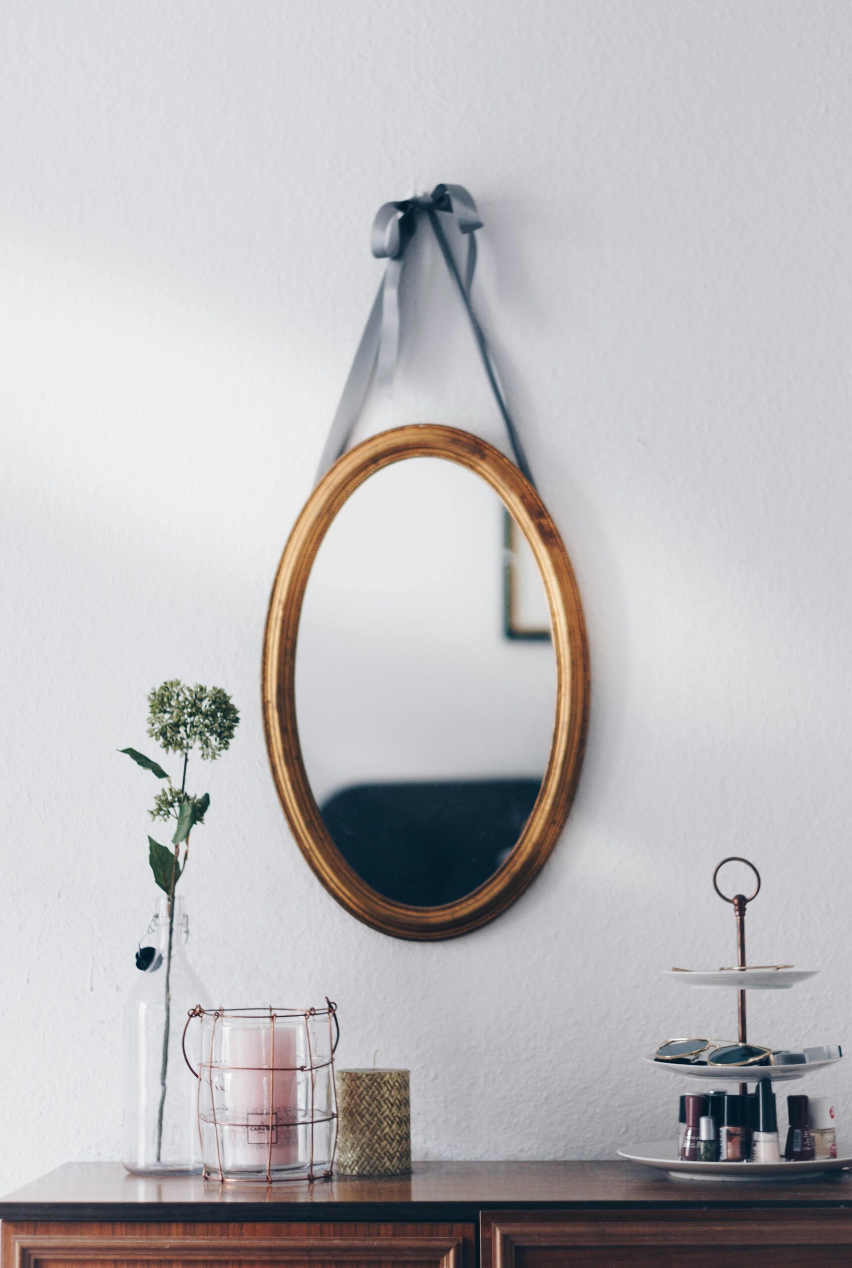A stylish interior setup featuring a hanging oval mirror with decorative elements on a wooden table.